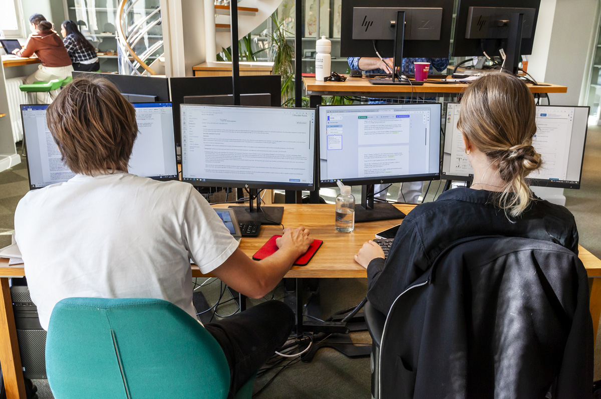 Två personer sitter och arbetar vid några datorskärmar.