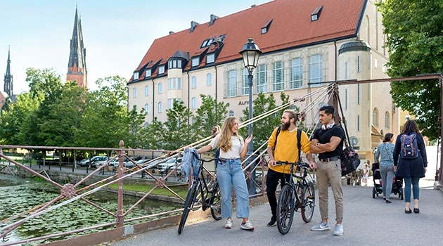 Three students walking with bicycles over a bridge in Uppsala. 