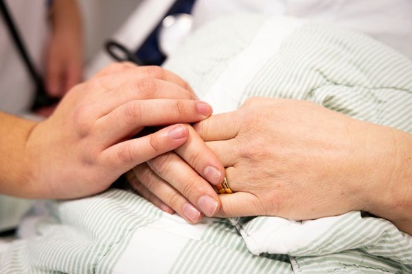 En handläggs på en patients händer i en sjukhussäng.