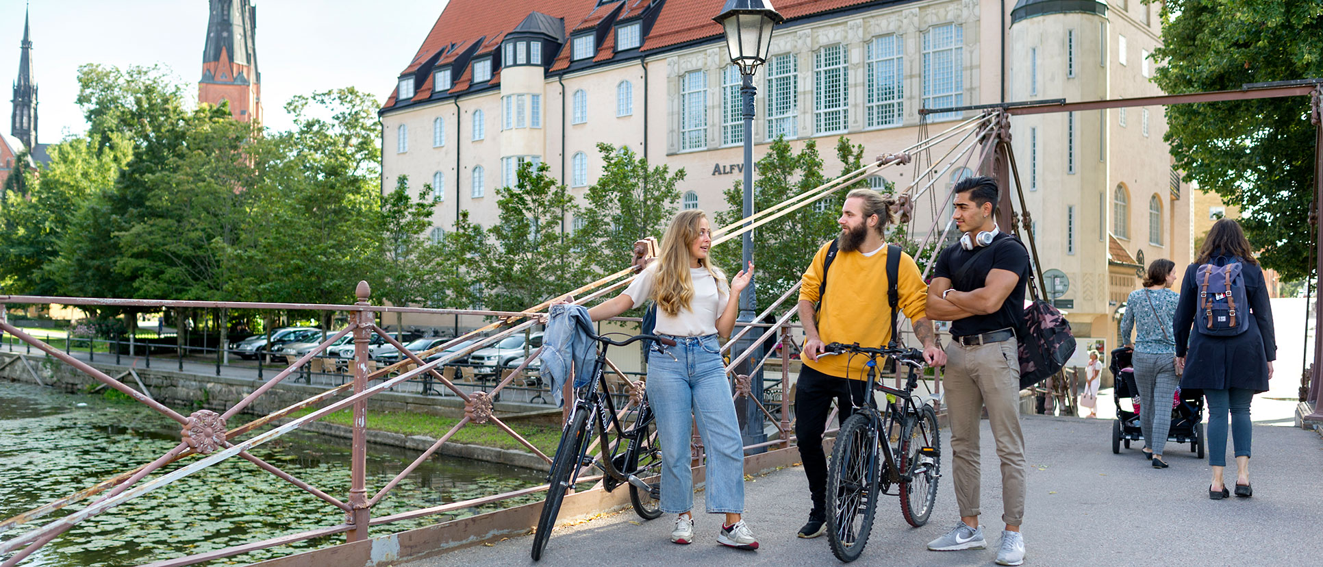 Studenter med cyklar går över en bro och pratar. 