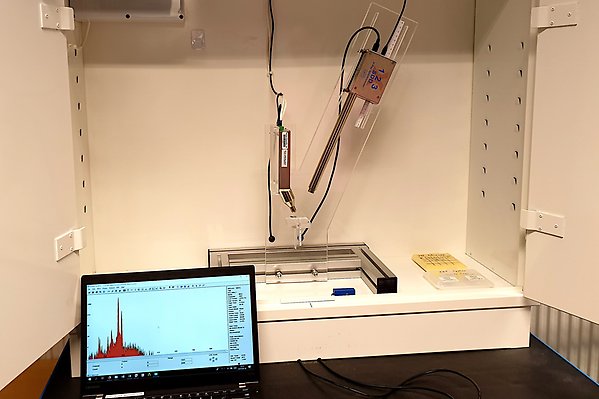 Röntgenfluorescensanordning i ett skåp. Röntgenkällan, detektorn och provhållaren är monterade på en plexiglasram. En bärbar dator som visar ett uppmätt spektrum står längst fram.