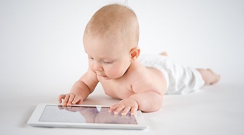 Baby lying on their stomach and looking at an iPad.