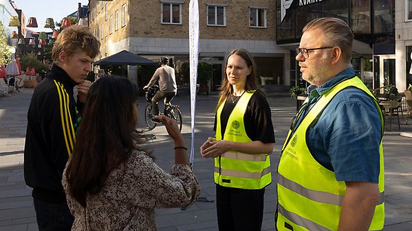 Två personer i gula västar pratar med två andra personer.