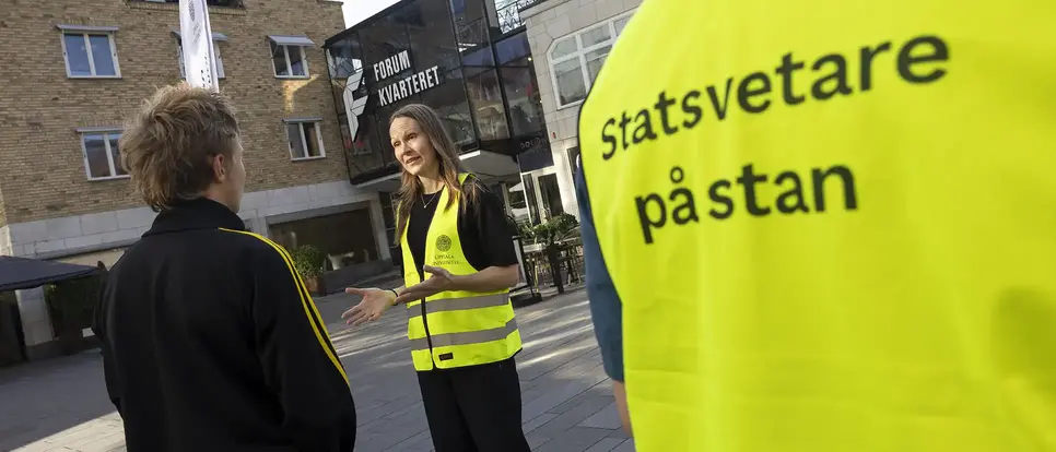 Två personer diskuterar på ett torg.