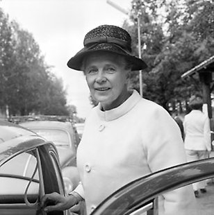 Svartvit bild av Alva Myrdal som är på väg in i en bil.