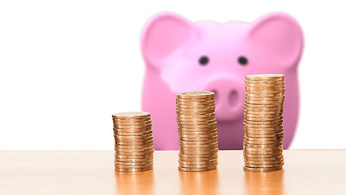 A pink piggy bank behind three stacks of coins. Source: Pixabay.