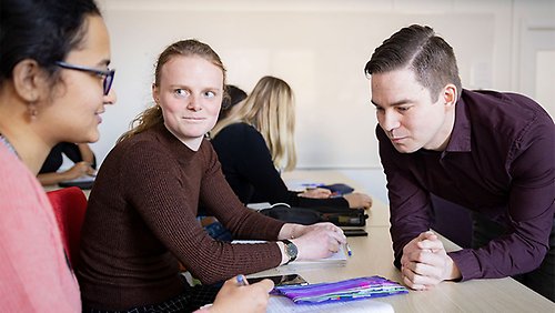 En kvinnlig student som tittar på en annan kvinnlig student till vänster. Till höger i bild en manlig lärare.
