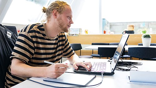 En manlig student som tittar på en dator och skriver på en skrivplatta.