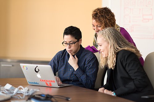 Tre kvinnor som står framför en laptop och pratar glatt