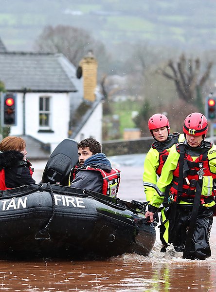 Räddningspersonal drar gummibåt med personer i på en översvämmad väg.