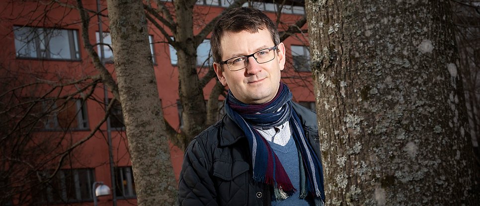 Daniel Brandell står vid ett lövfritt träd utanför Ångströmslaboratoriet.