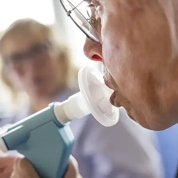 En äldre person har en inhalationsapparat i munnen.