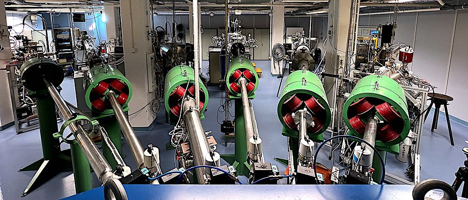 Vy från switchmagnetens position in i experimenthallen i Tandemlaboratoriet. Sex strålrör sträcker sig in i rummet. Deras tydligaste kännetecken är gröna och röda magneter.