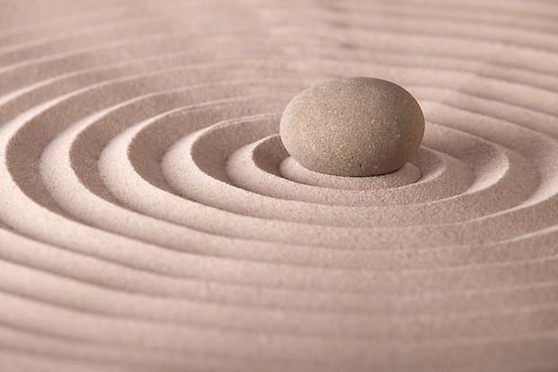 Bilden föreställer en sten i sand med ringar av sand som omsluter den