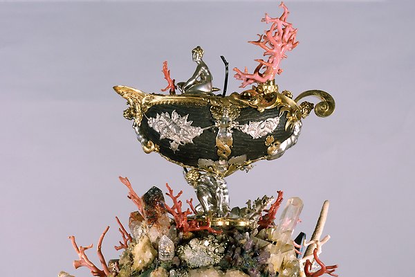 En seychellnöt smyckad med gyllene detaljer och stenar. Högst upp sitter en silverfärgad figur som föreställer en människa.