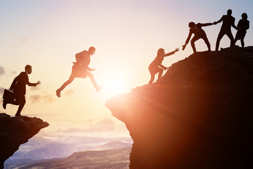 Grupp personer i kontorskläder som klättrar på ett berg och hjälper varandra uppåt. Foto: Gettyimages