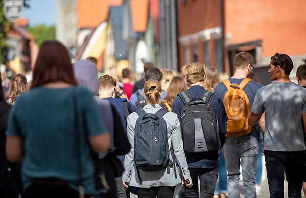 Many students walking on a street in Visby. They are carrying backpacks.