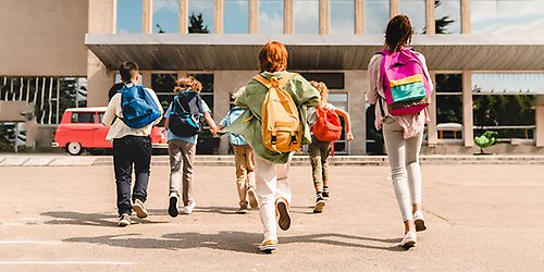 Barn springer mot sin skola. De har färgglada ryggsäckar.