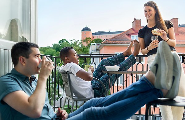 three students having a snack on a balcony in Uppsala with a view of the castle
