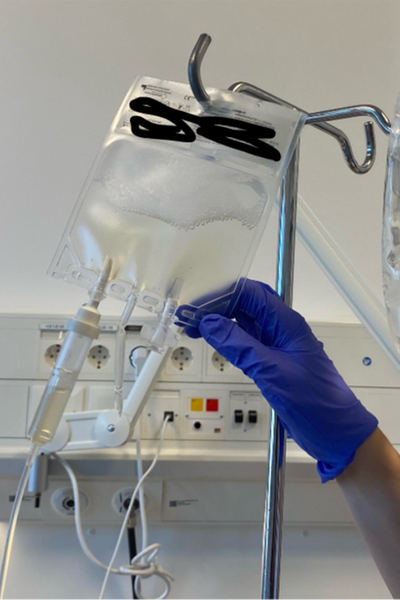 En hand med en lila skyddhandske håller i en droppåse