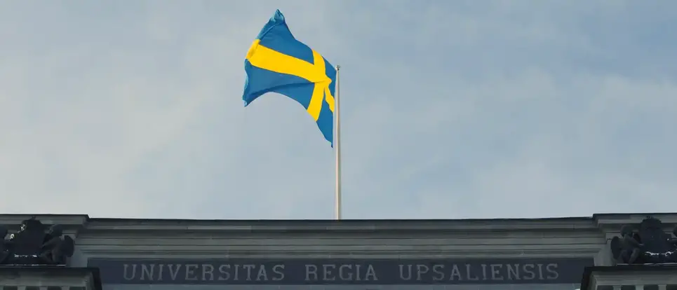 The Swedish flag flying at the top of the university main building’s roof, with the words “Universitas regia upsaliensis” on the façade