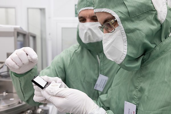 två forskare i gröna overaller och munskydd undersöker liten pryl