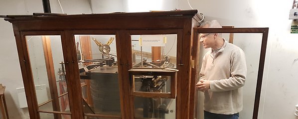 Björn lund som tittar in i trä och glaskabinettet i vilket Wiechert-seismografen i Uppsala står.