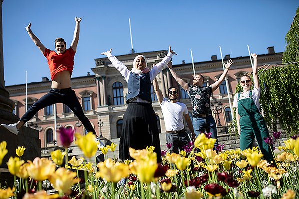 Bilden visar studenter som hoppar upp i luften framför universitetshuset. I förgrunden syns gula tulpaner