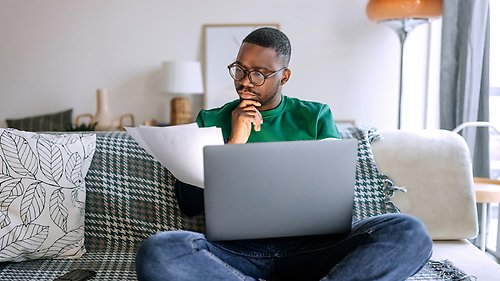 Person sitting on a couch with a laptop and some papers.