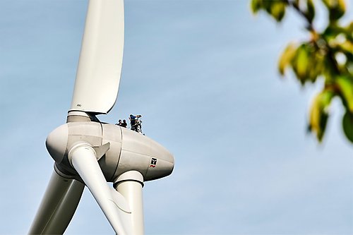 Two persons standing on top of a wind turbine
