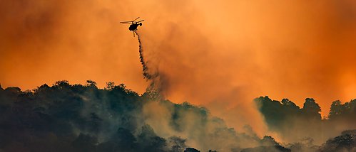 En helikopter flyger över ett rykande landskap och släpper vatten.