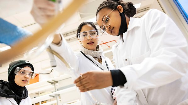 Three women working in a lab in white lab coats. 
