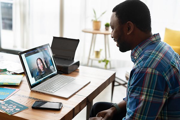 En person sitter vid ett skrivbord med en laptop framför sig, genom vilken ett videosamtal med en annan person förs.