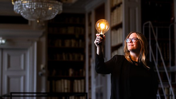 Marika Nestor håller i en lysande glödlampa i ett bibliotek. 