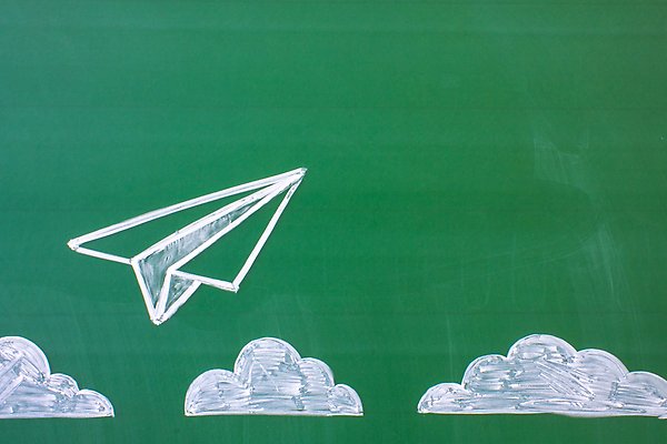 Blackboard where someone has drawn clouds and a paper airplane.