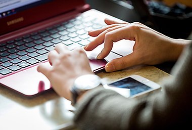 Bild på händerna på en person som sitter vid en röd laptop.