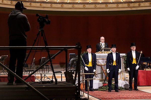 The Vice Chancellor gives a speech at the podium in the university hall. In front of him stand the three people who are part of the ceremonial guard.