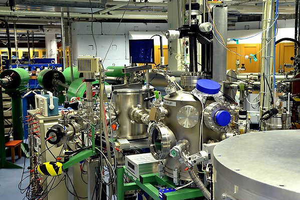 The end station of beamline 4. Two vacuum chambers are fully visible, and the edge of a third one is photographed in the right lower corner. Several measurement instruments and many cables can be seen. In the back, the blue switching magnet is visible. Besides beamline 4 with two green magnets, the starting points of other beamlines can be seen.