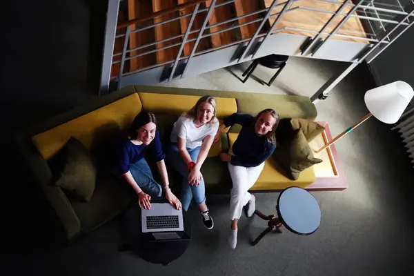 Tre personer sitter i en stor soffa. En av personerna har en laptop i knät.