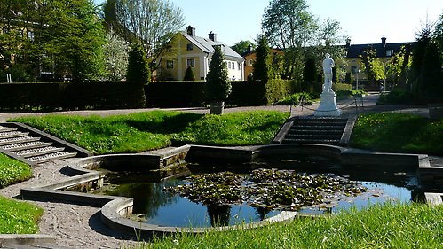 En damm och en skulptur omgivna av grönska i Linnéträdgården
