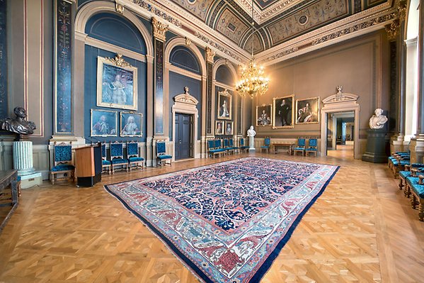 Chancellor's room with an oriental rug in the middle, antique chairs along the walls, a lectern, busts in the corners, and painted portraits on the walls