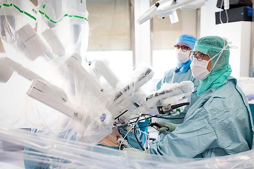 Two persons in scrubs operating a plastic covered robot in an operating theatre.