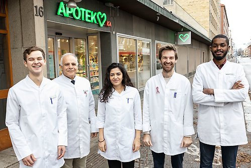 Five pharmacists standing outside of a pharmacy in lab coats.