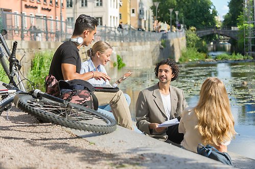 Four students sitting by Fyrisån in Uppsala chatting
