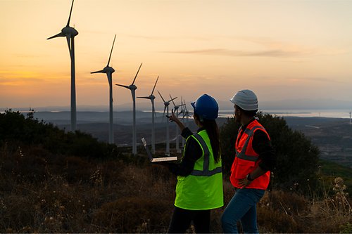 Two people pointing at wind turbines in the sunset