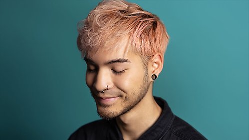 Student portrait in front of green background. The student has pink hair and has closed eyes.