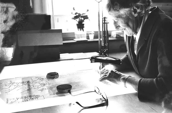 Gerd Enequist, roughly 65 years old, at a drawing table with a map and a magnifying lamp.