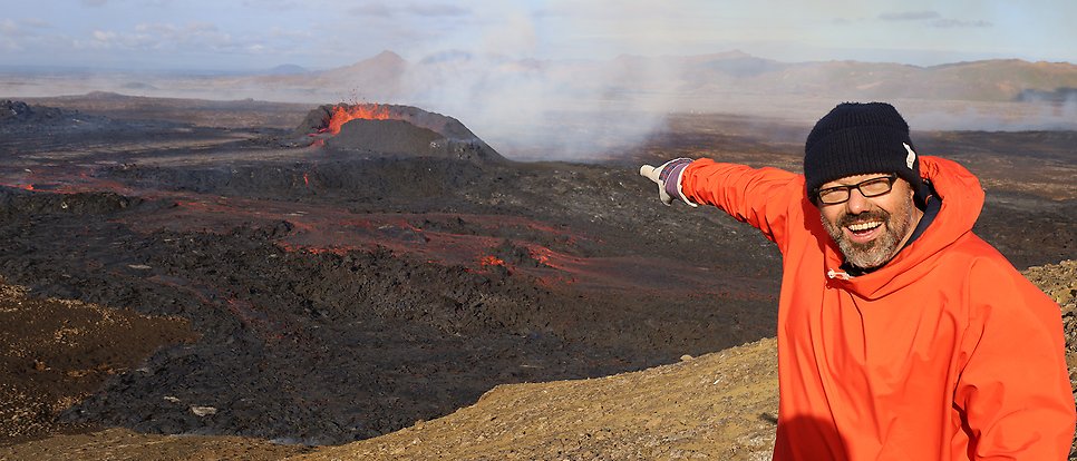 Valentin Troll on Iceland pointing at an erupting volcano.