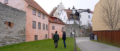 två personer går bland gamla byggnader i Visby.