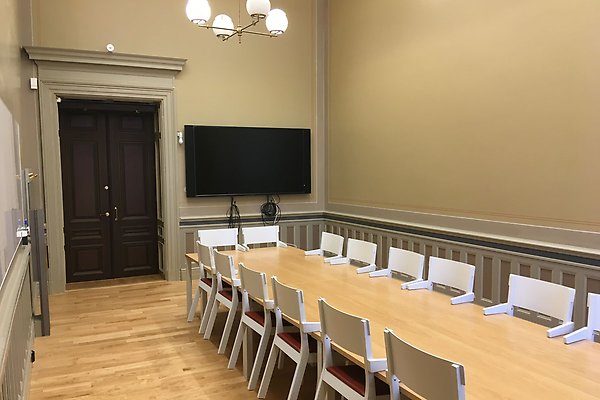 Ett seminarierum med ett bord, stolar och en brun dörr.